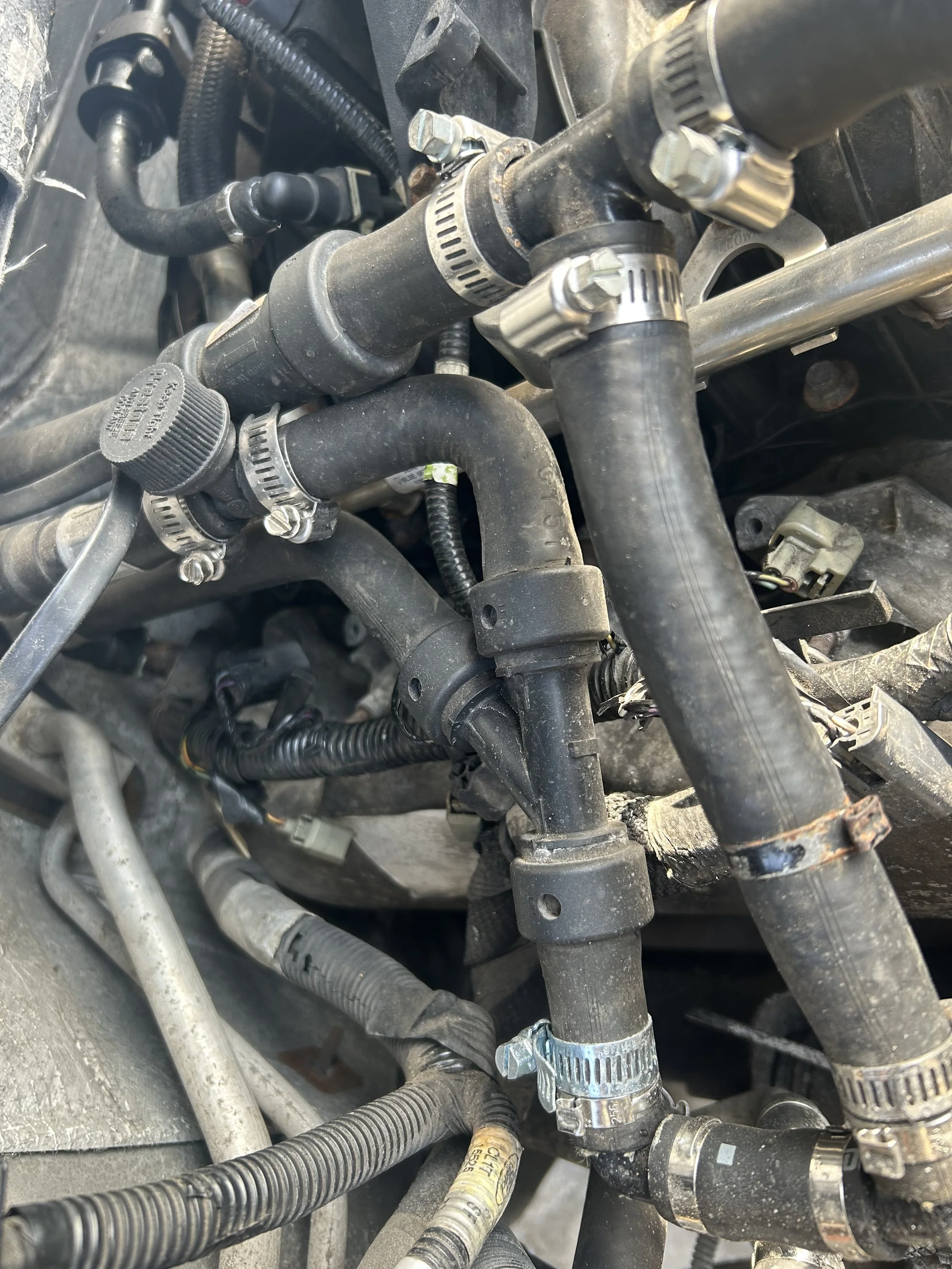 Close-up of a complex network of engine hoses, clamps, and fittings, showing various metal and rubber components with some dirt and wear.