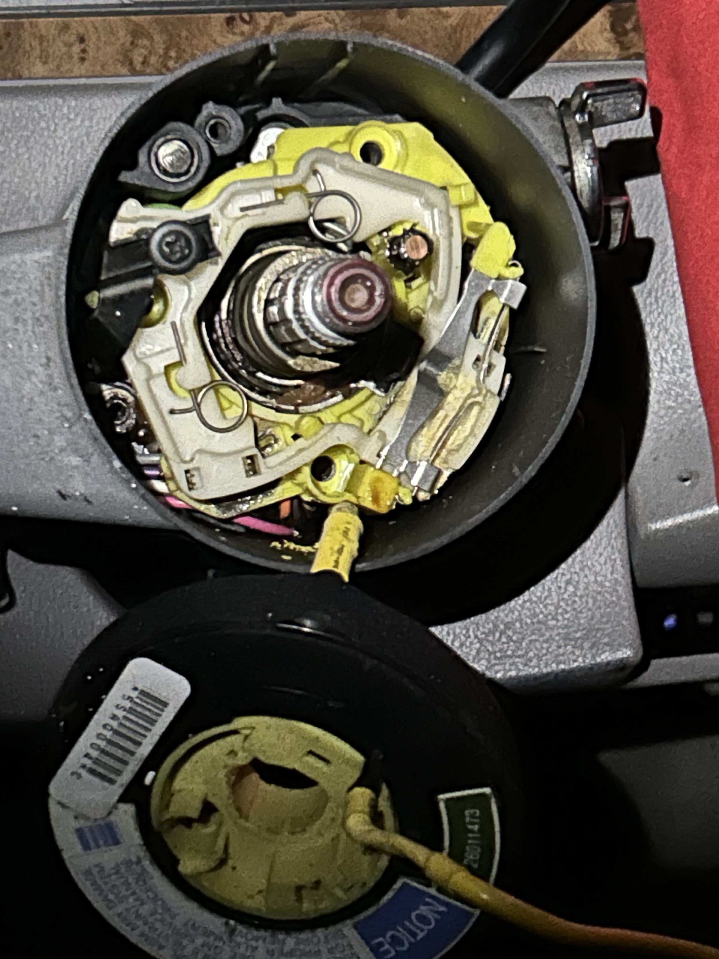 Close-up of a disassembled mechanical component, possibly a part of an engine or machinery, with visible wiring, gears, and metal parts on a work surface.