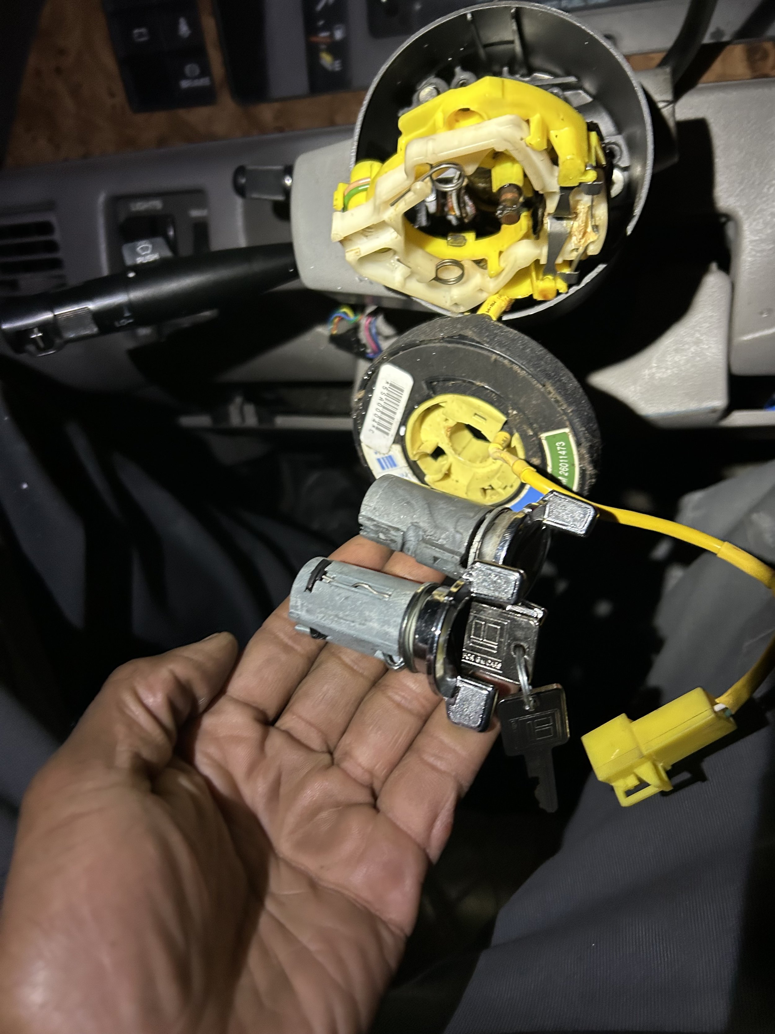A mechanic holding a mechanical part over a vehicle dashboard panel with exposed electrical components and wiring.