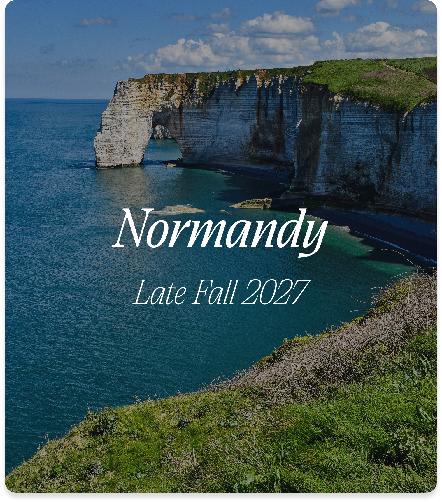Cliffs and coastline of Normandy, France with a notable arch-shaped rock formation in the sea, under a partly cloudy sky, with green grassy and shrub-covered foreground.