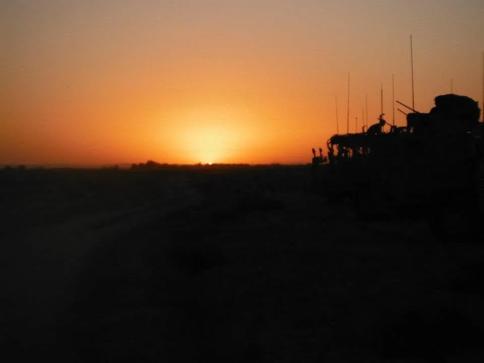 Silhouette of military vehicles at sunset or sunrise with an orange sky.