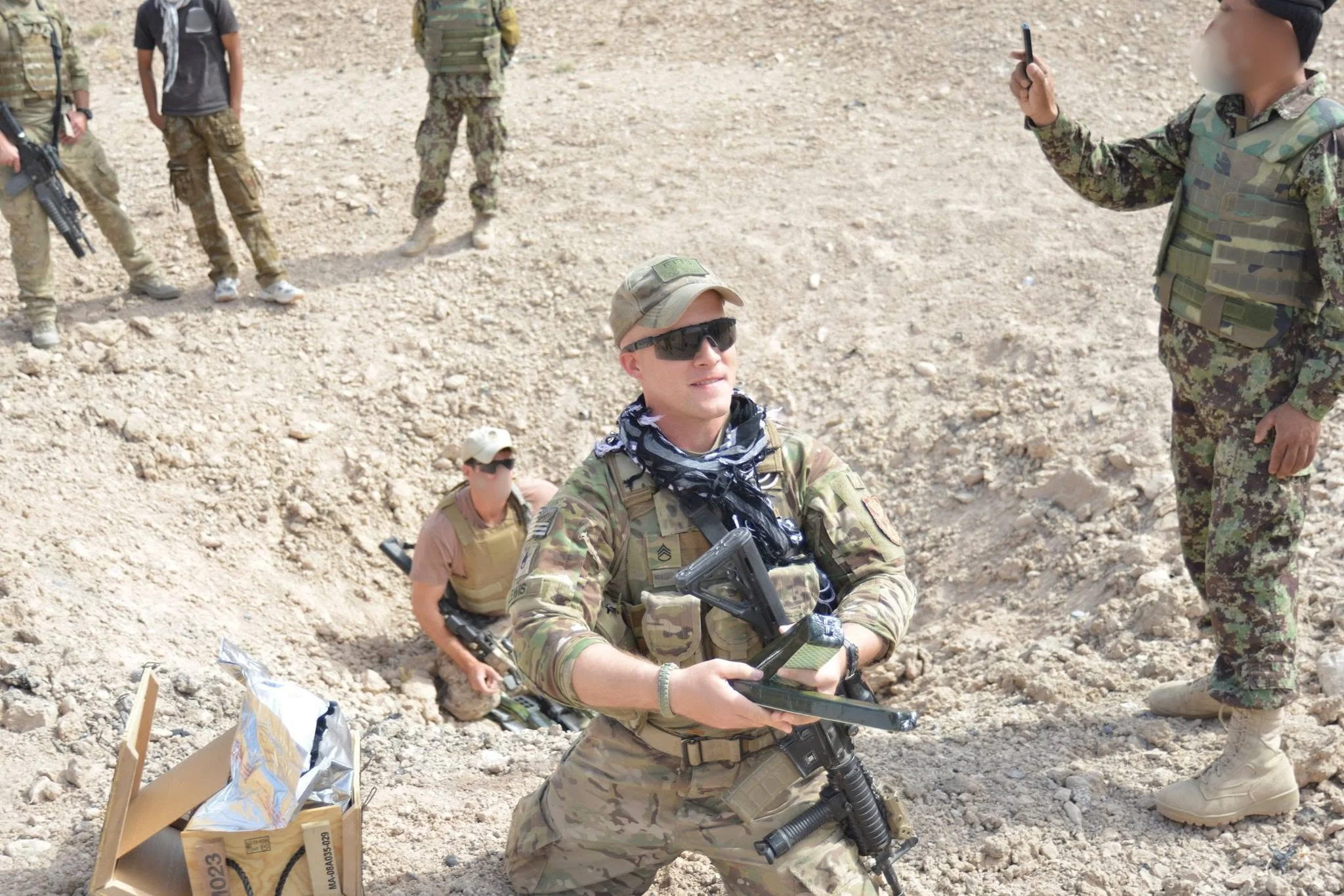 Military personnel in camouflage uniforms participating in an outdoor activity on rocky terrain, with some holding equipment and others observing.