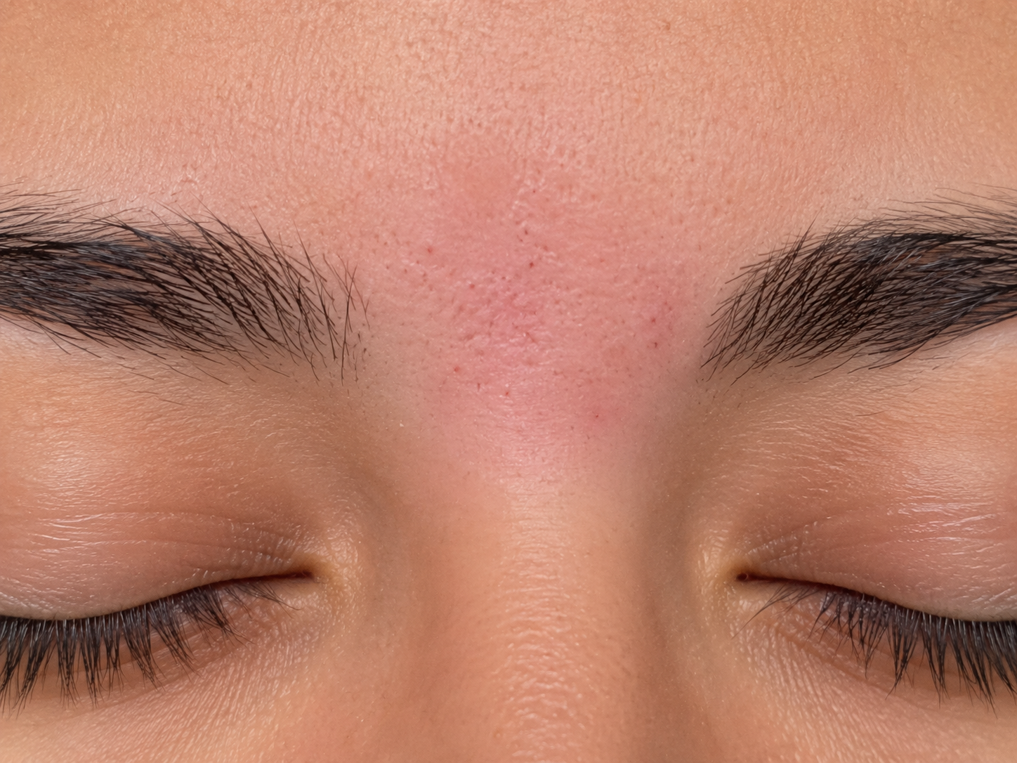 Close-up of a person's forehead and eyebrows with closed eyes, showing skin texture and facial hair.