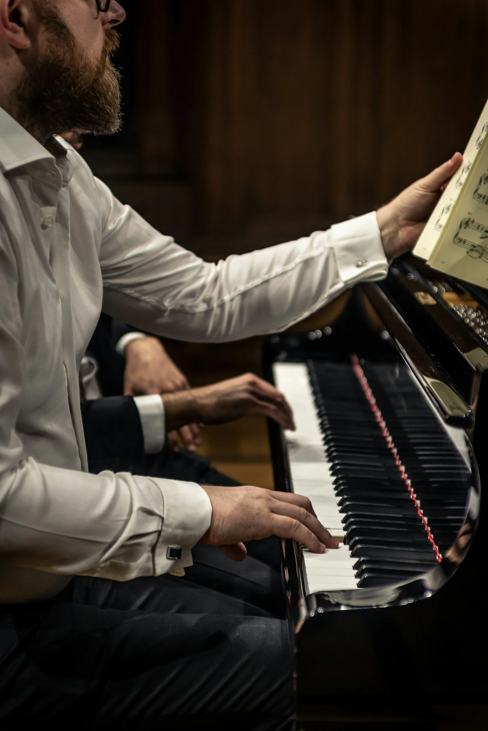 Close-up of two people playing a grand piano, with sheet music on the stand.