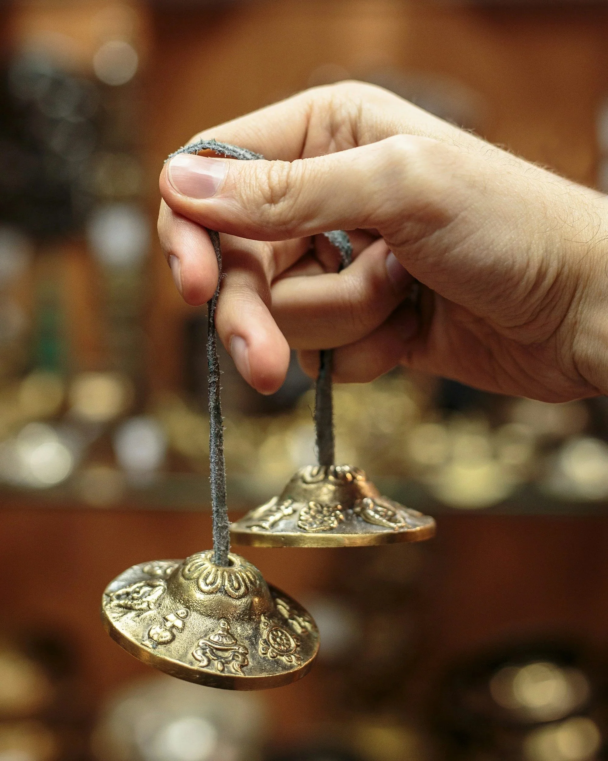 Close-up of a hand holding an ornate, decorative metal bell with intricate floral patterns, hanging by a string.