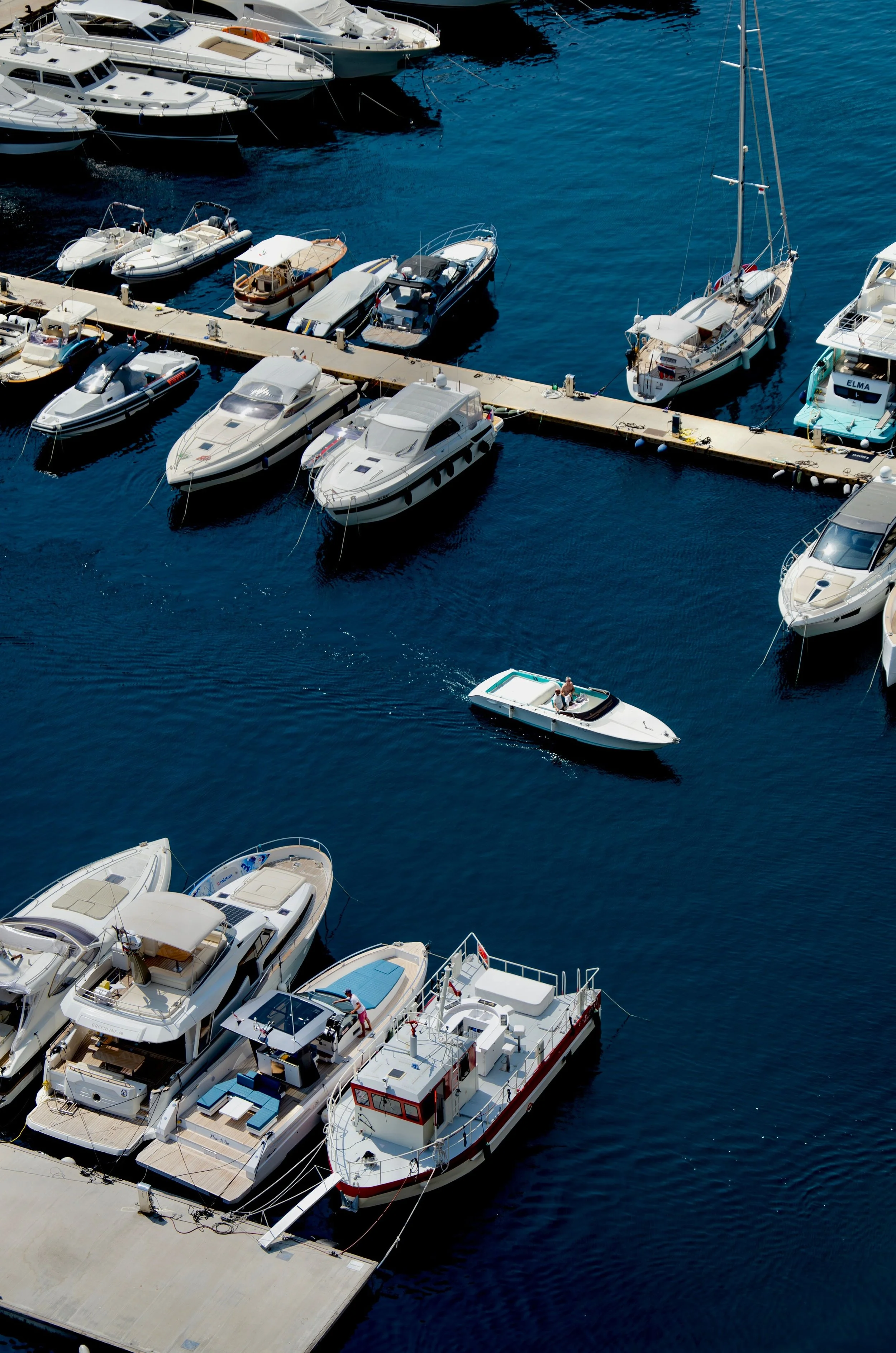 Several boats and yachts are docked at a marina with a woman on a small motorboat on the water near the dock.