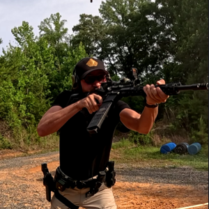 Man aiming a rifle outdoors with trees in the background