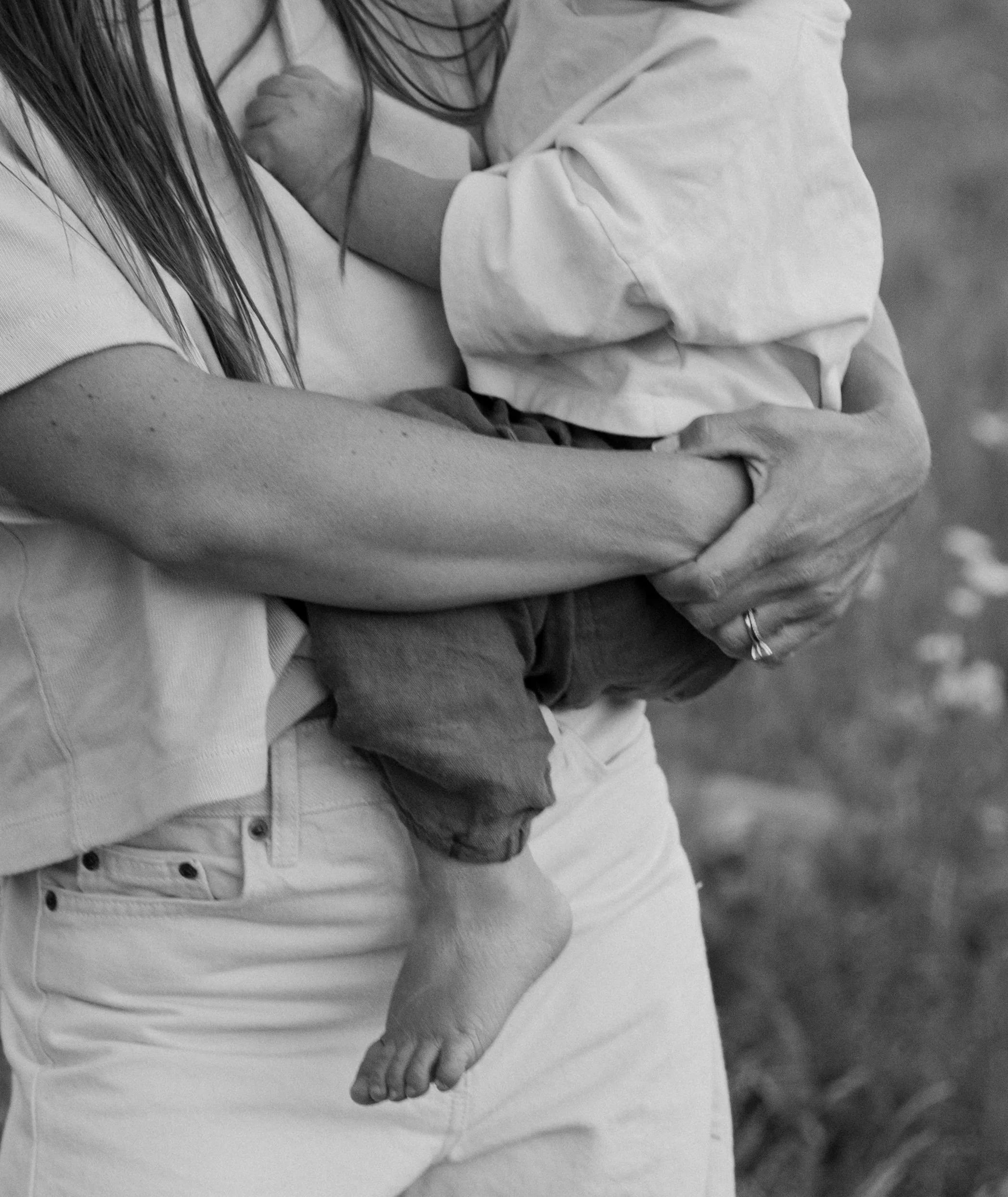 A close-up black-and-white photo of a person holding a child, with the child's hand resting on the person's arm, showing a tender moment.