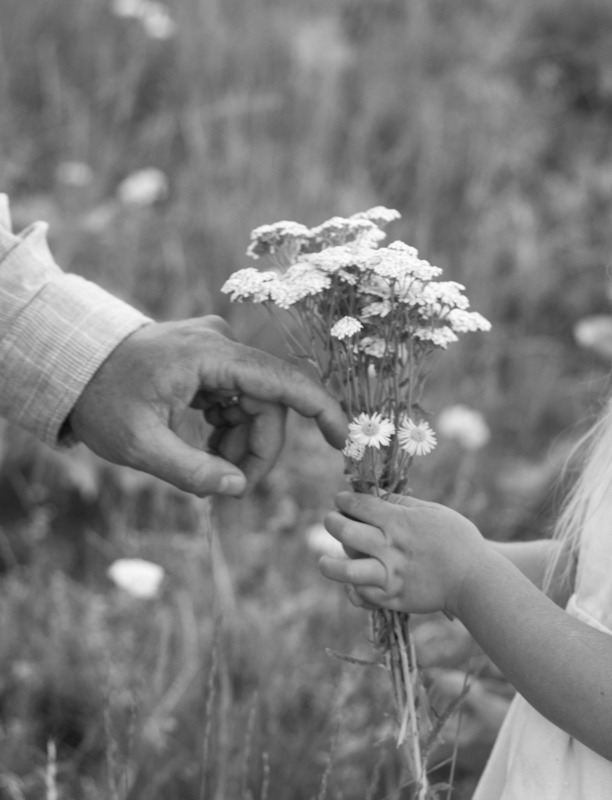 Two children are exchanging a bouquet of wildflowers outdoors, with one child handing the bouquet to the other.