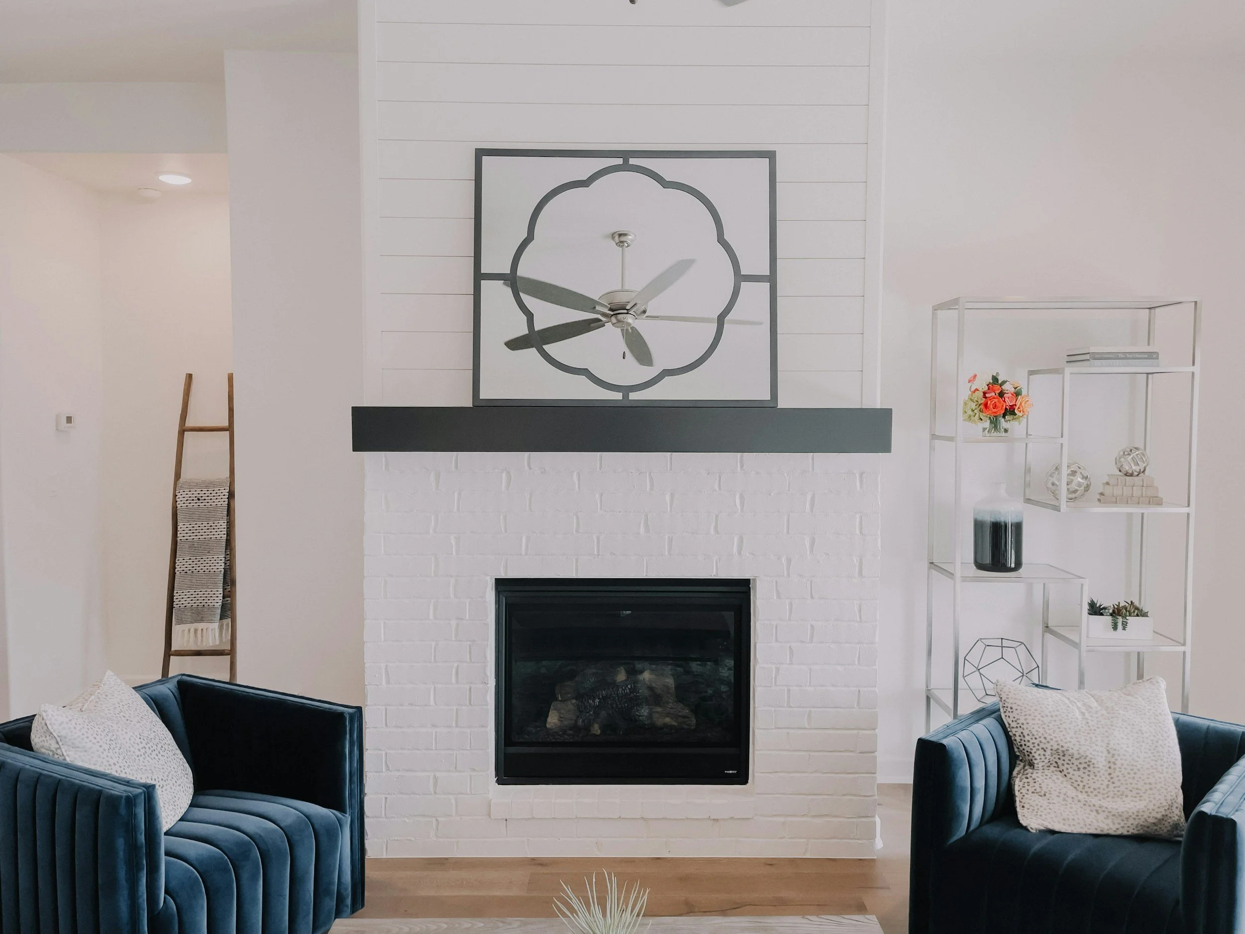 A living room with a white shadow box mantel, a black fireplace, and white shiplap walls. 