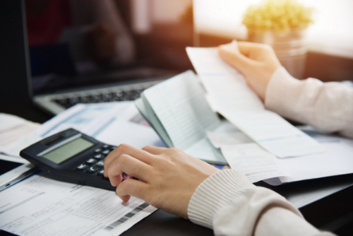 Person working at a desk with a calculator, papers, an open notebook, and a laptop.