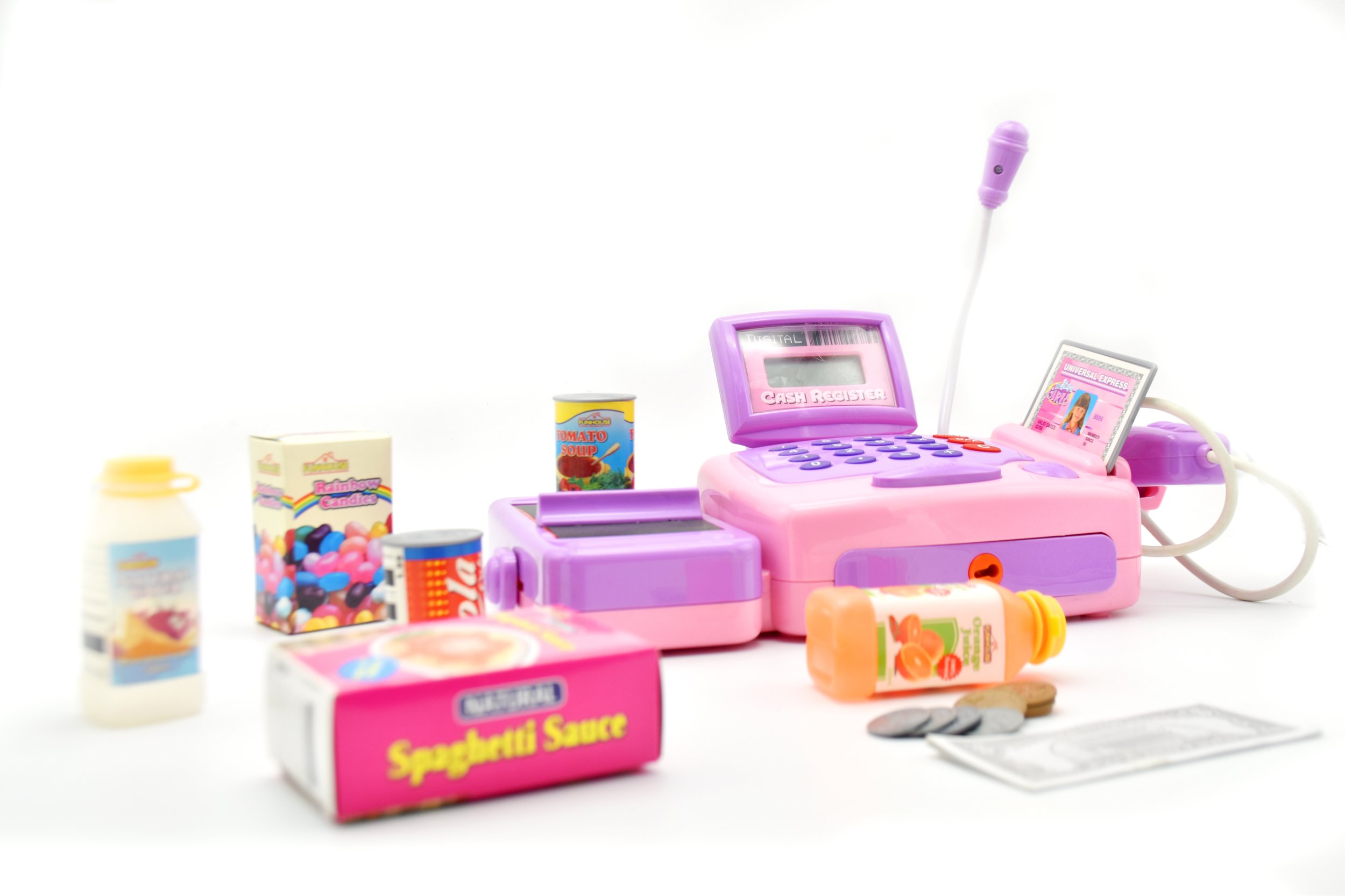 Pink toy cash register with toy food items and pretend credit card, surrounded by small containers of play food like soup, candies, and juice boxes, on a white background.