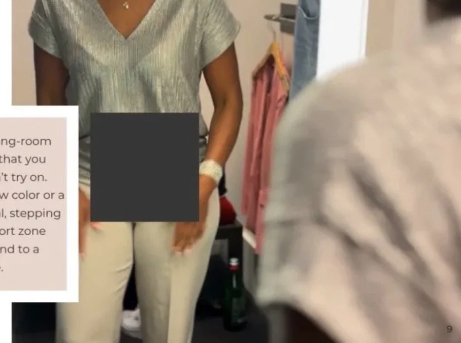 A woman wearing a light-colored top and pants standing in a clothing fitting room with a pink garment hanging nearby, and a partial view of a person in a striped shirt.