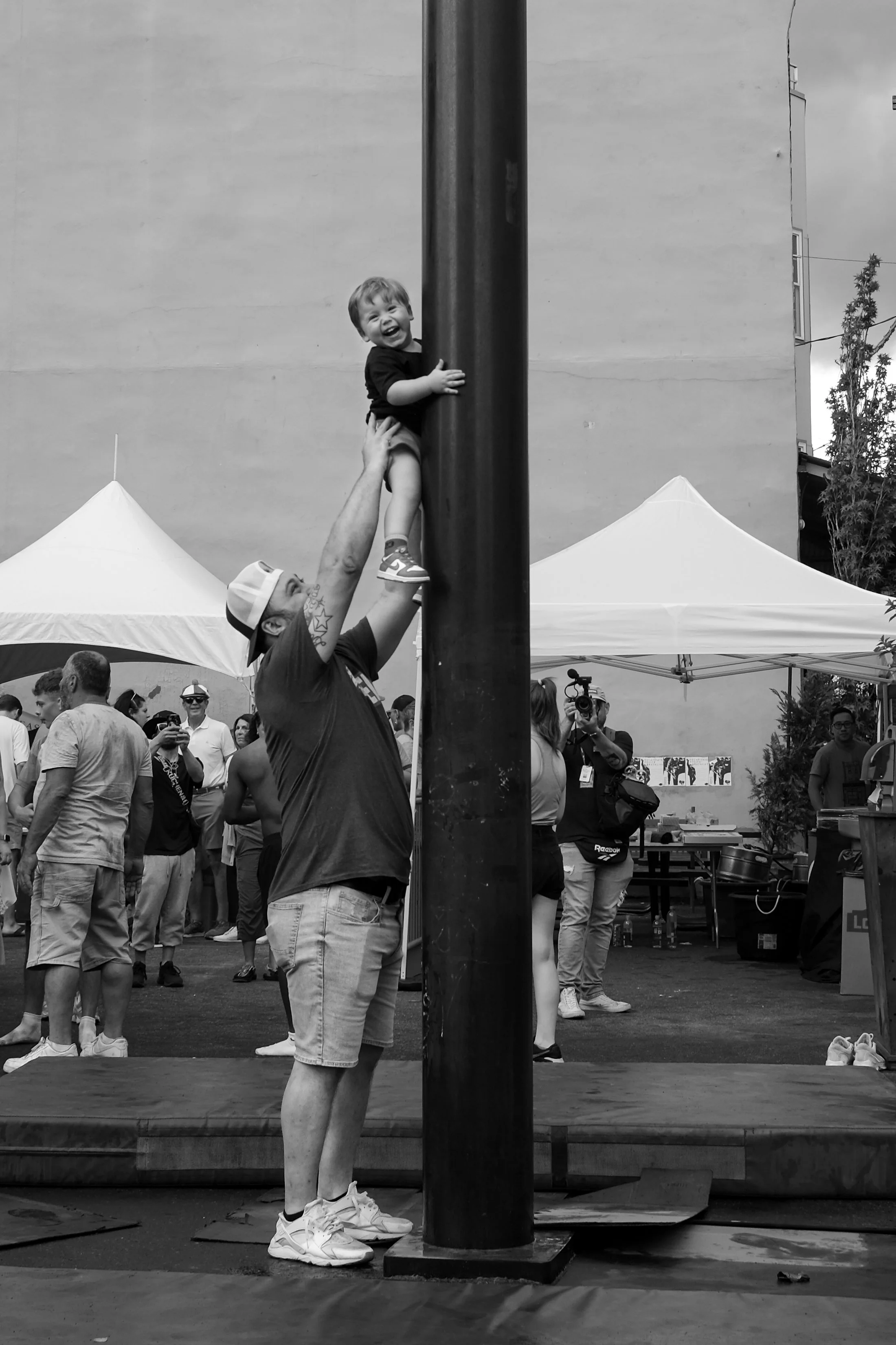 Father lifts his son during the greased pole climbing competition at the Italian Market Festival in Philadelphia, Pa. in May 2025.