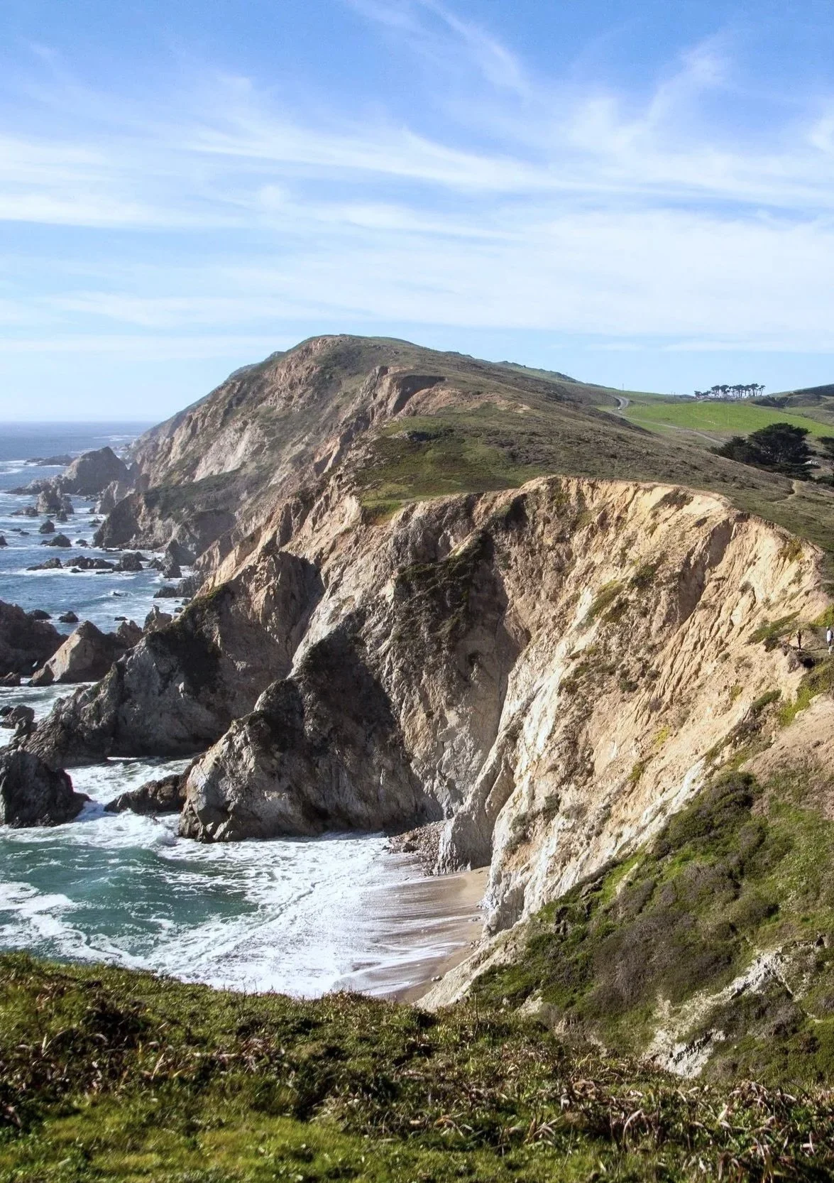 Coastal cliffs with rocky shoreline, grassy areas, and a blue sky with clouds.