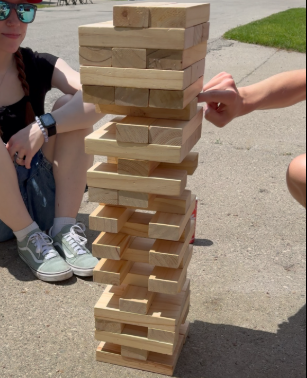 Children playing a large wooden Jenga game outdoors on a sidewalk.