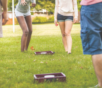People playing cornhole outdoors on a grassy field.