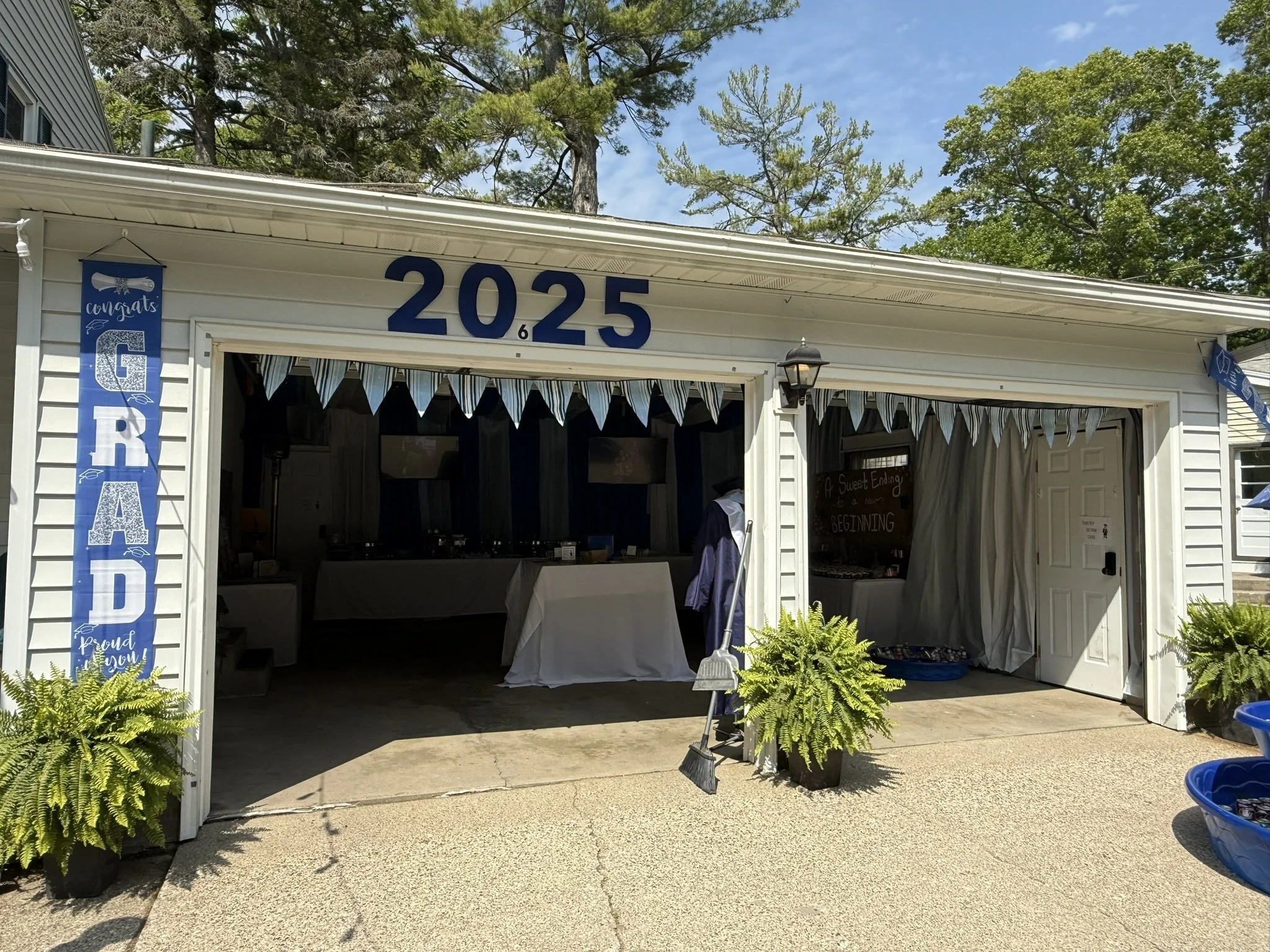The exterior of a garage decorated for a graduation celebration with blue and white banners and flowers, displaying the year 2025.