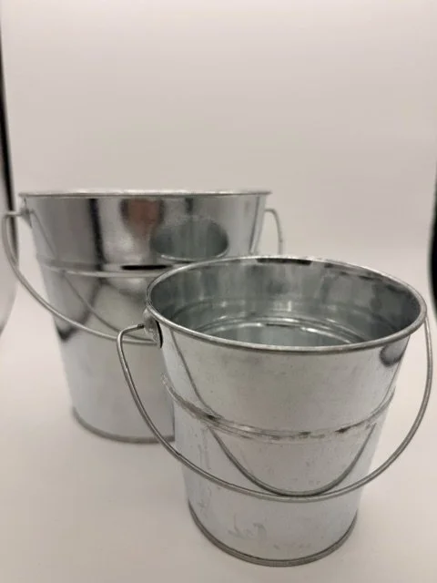 Two small metal buckets, one behind the other, on a plain background.