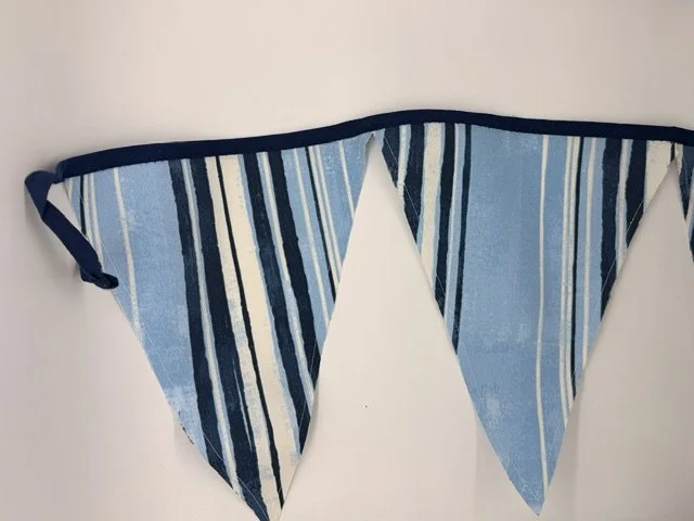 A blue, white, and navy striped fabric pennant banner hanging on a white wall.