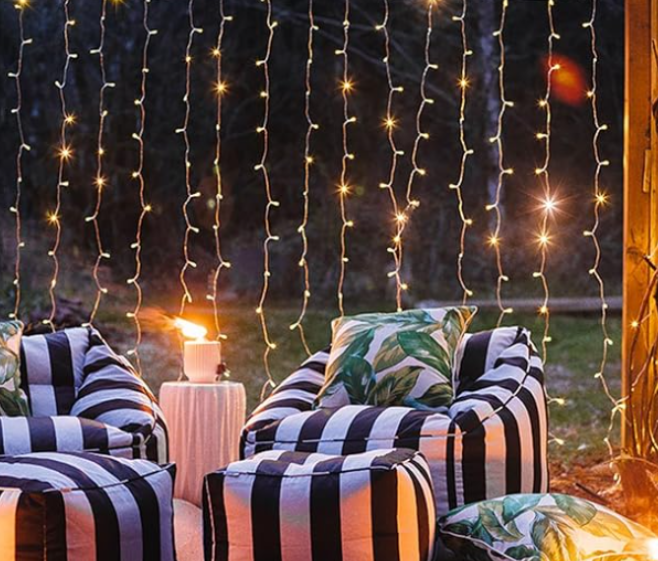 Outdoor seating area with two striped armchairs, a small wooden table with a candle, and string lights hanging overhead, set at night.
