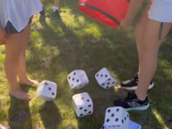 Two people, one with bare feet and the other with sneakers, standing on grass near large dice, some of which are in the air.
