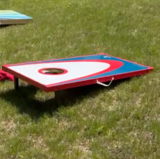 A cornhole game set up outdoors on grass, with a board featuring a hole for tossing bean bags.