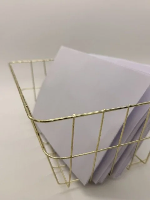 A gold wire basket filled with papers or documents placed on a white surface.