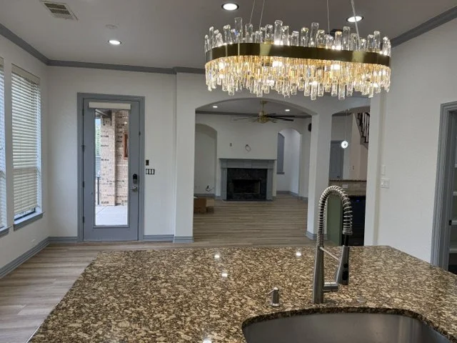 Modern kitchen with a granite countertop island, a chandelier, and a view into the living room with a fireplace.