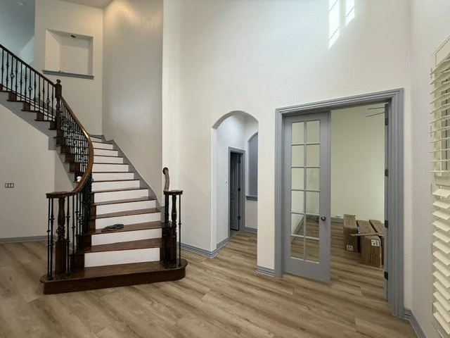 Empty living area with a curved staircase, hardwood floors, and an open doorway leading to another room with boxes.