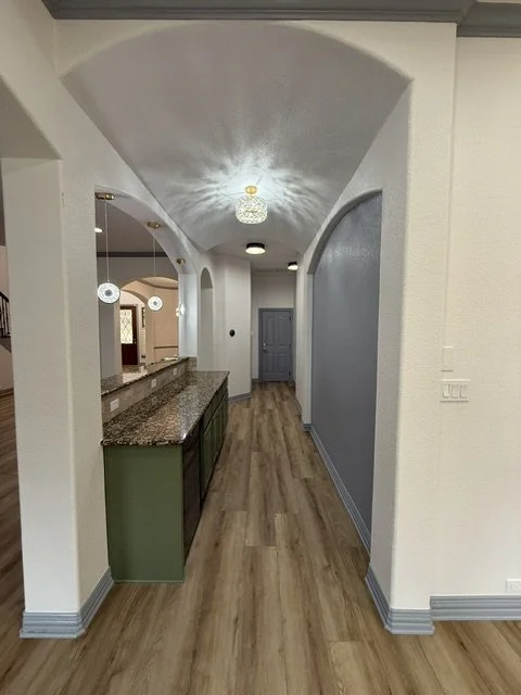 Interior view of a hallway with wooden floor, arched ceiling, and a granite-topped counter on the left. There are hanging pendant lights and a chandelier, with a blue door at the end of the hallway.