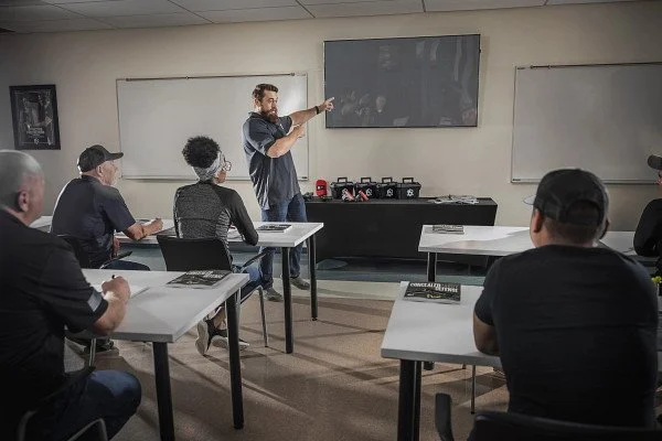 A classroom with a male instructor pointing at a blackboard, teaching a group of students seated at desks.