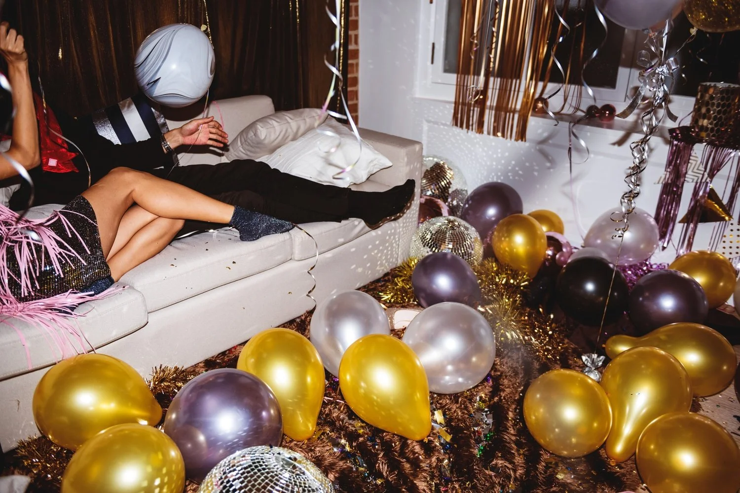 Party room with balloons, decorations, and people celebrating on a couch.