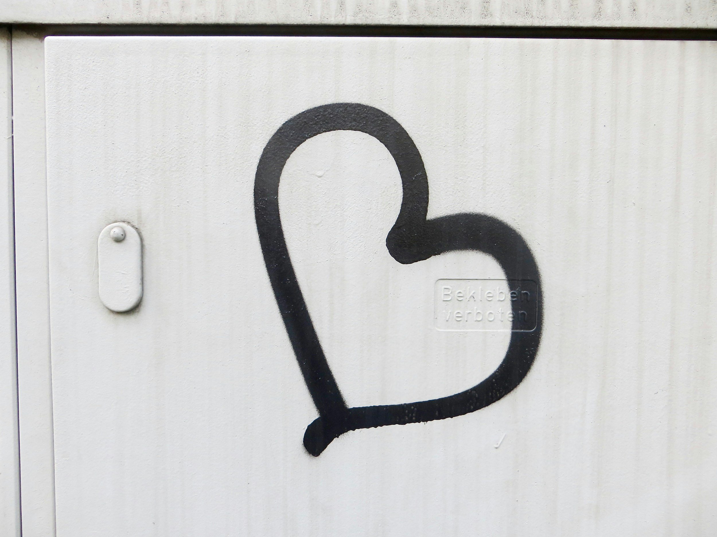 Close-up of a graffiti drawing of a light bulb on a white metal surface, with a small plaque that reads 'Beleuchtung verboten' indicating lighting is prohibited.