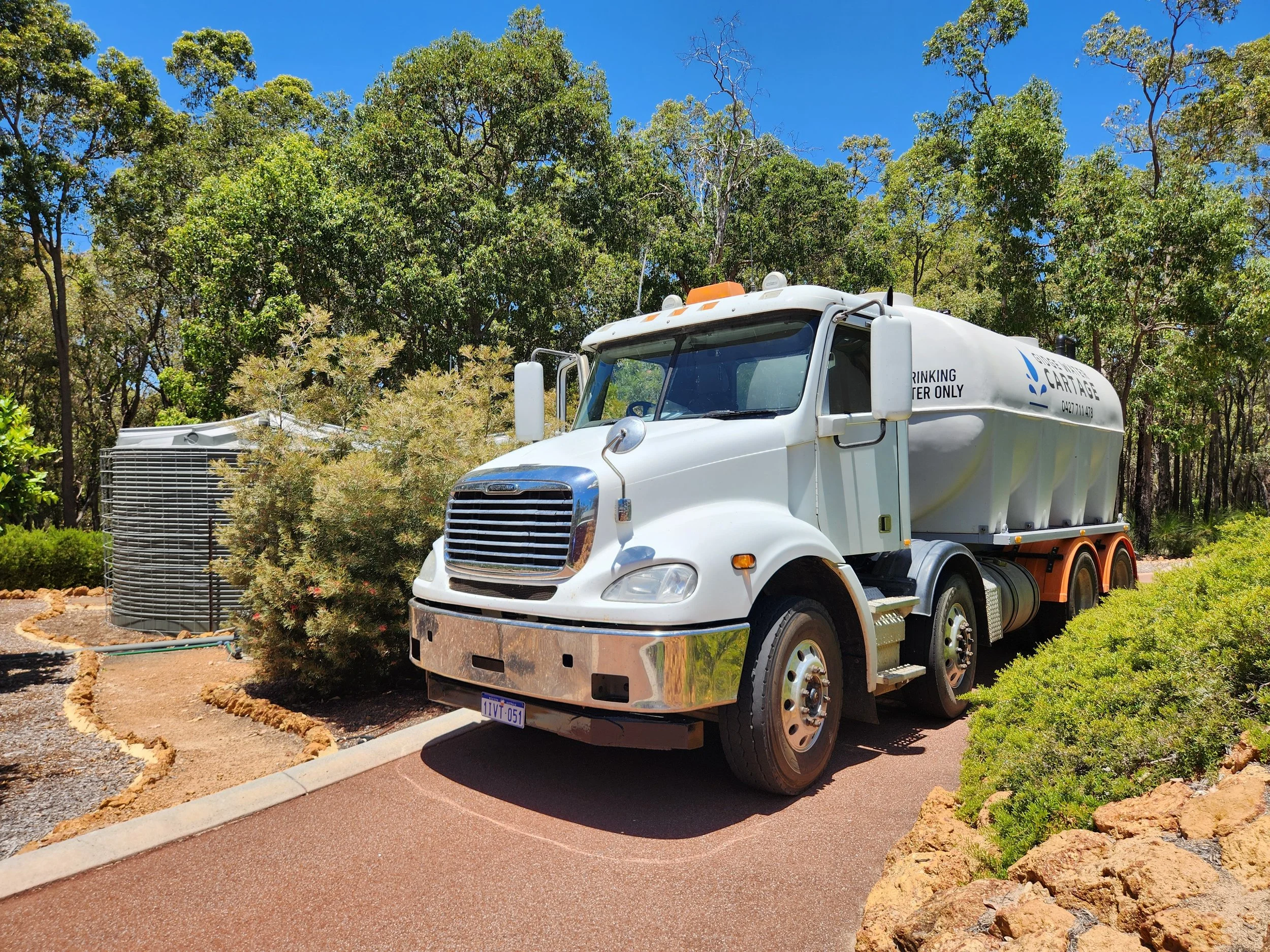 A white utility truck parked on a paved surface with green trees and blue sky in the background.