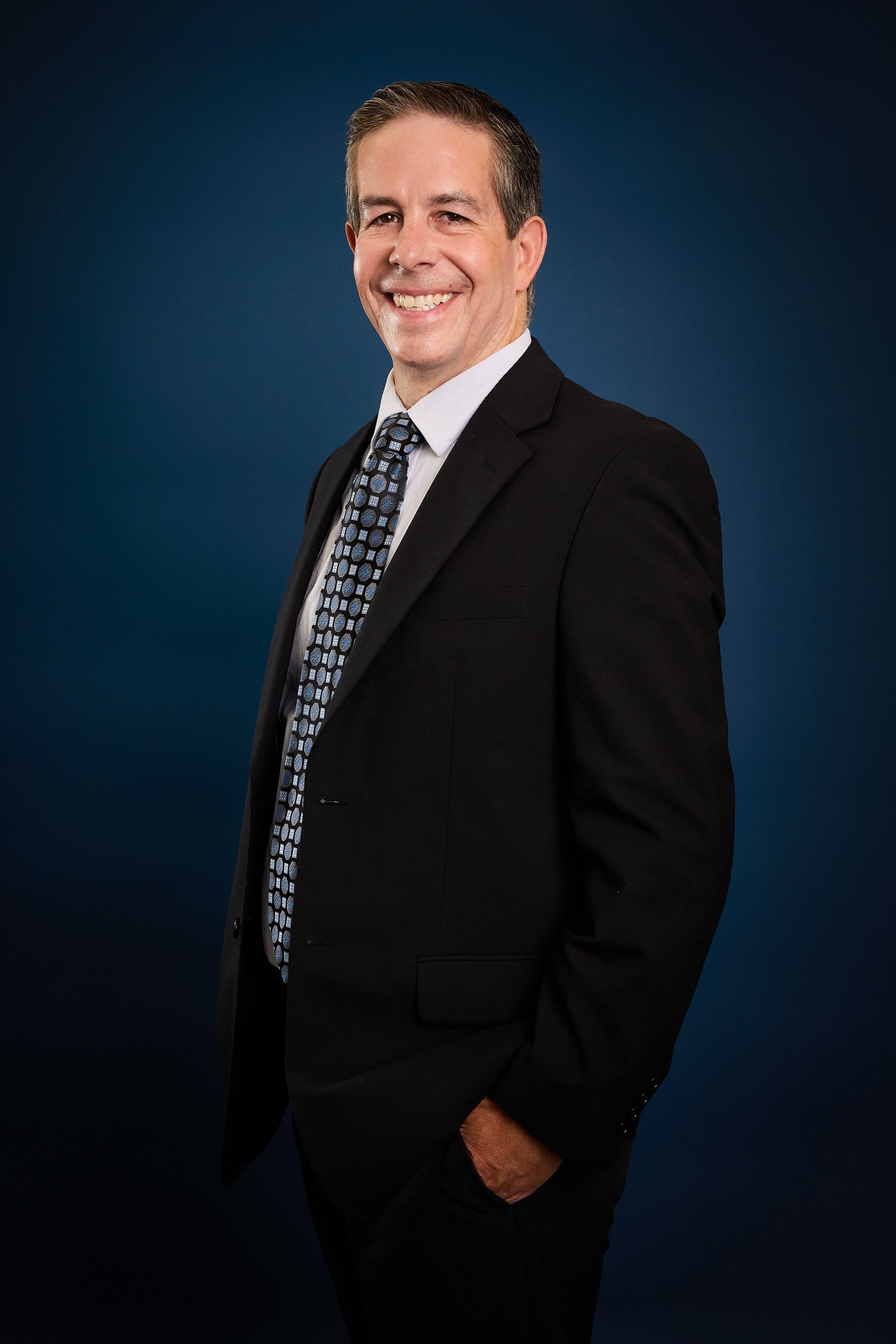 Portrait of a smiling man in a business suit with a dark blue background.