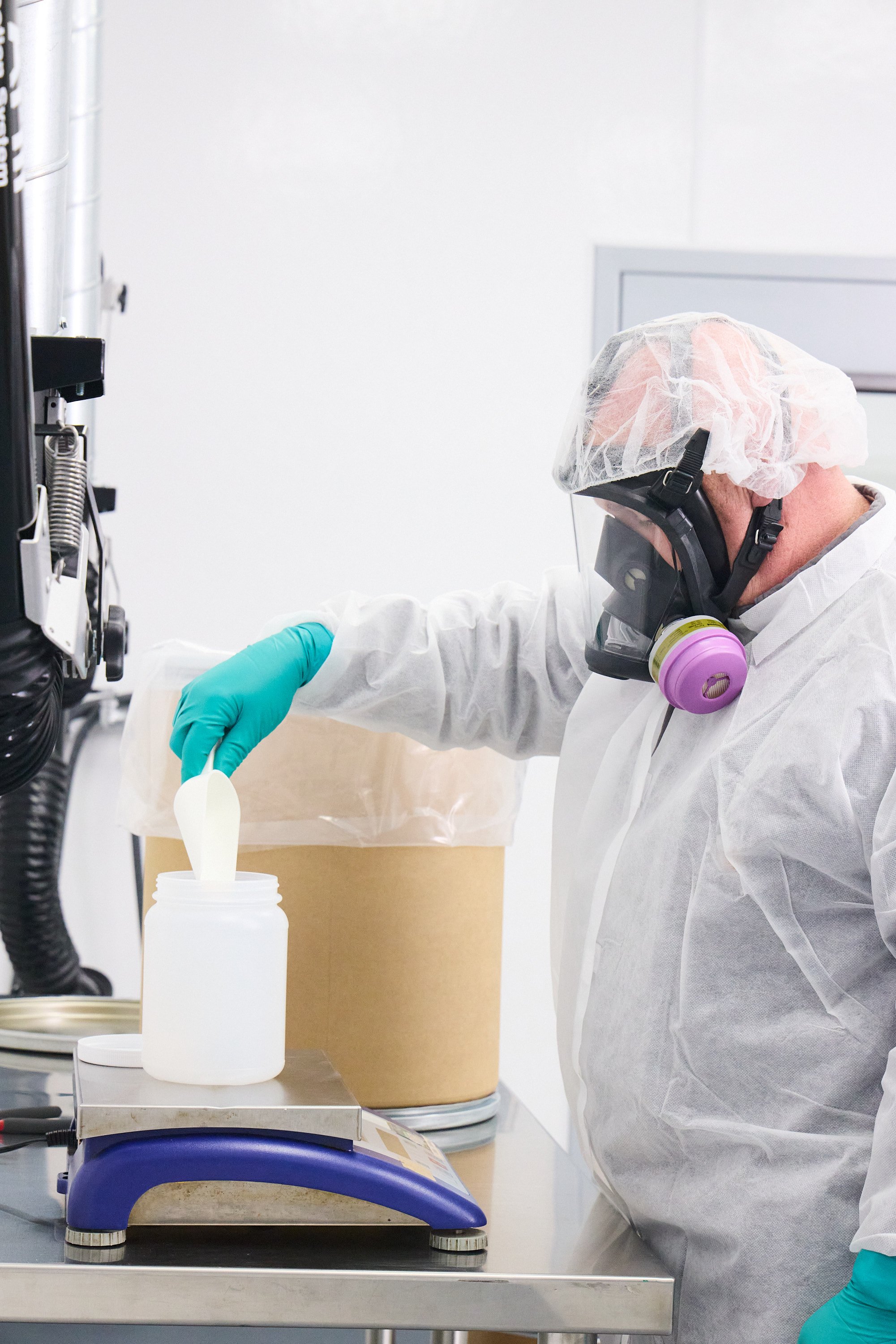 A scientist in protective clothing handling a container in a laboratory setting.