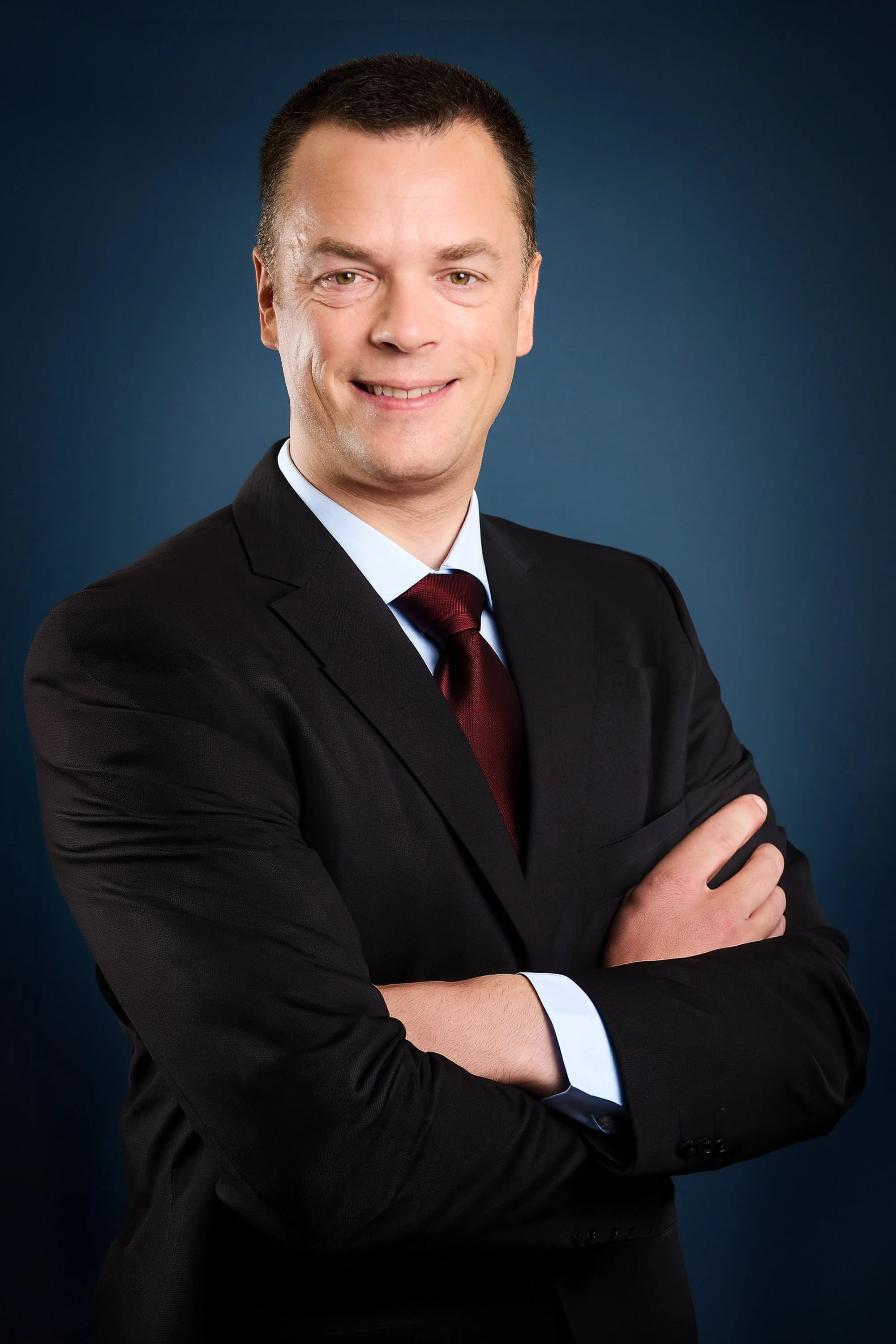 Professional man in a suit with crossed arms smiling against a blue background.