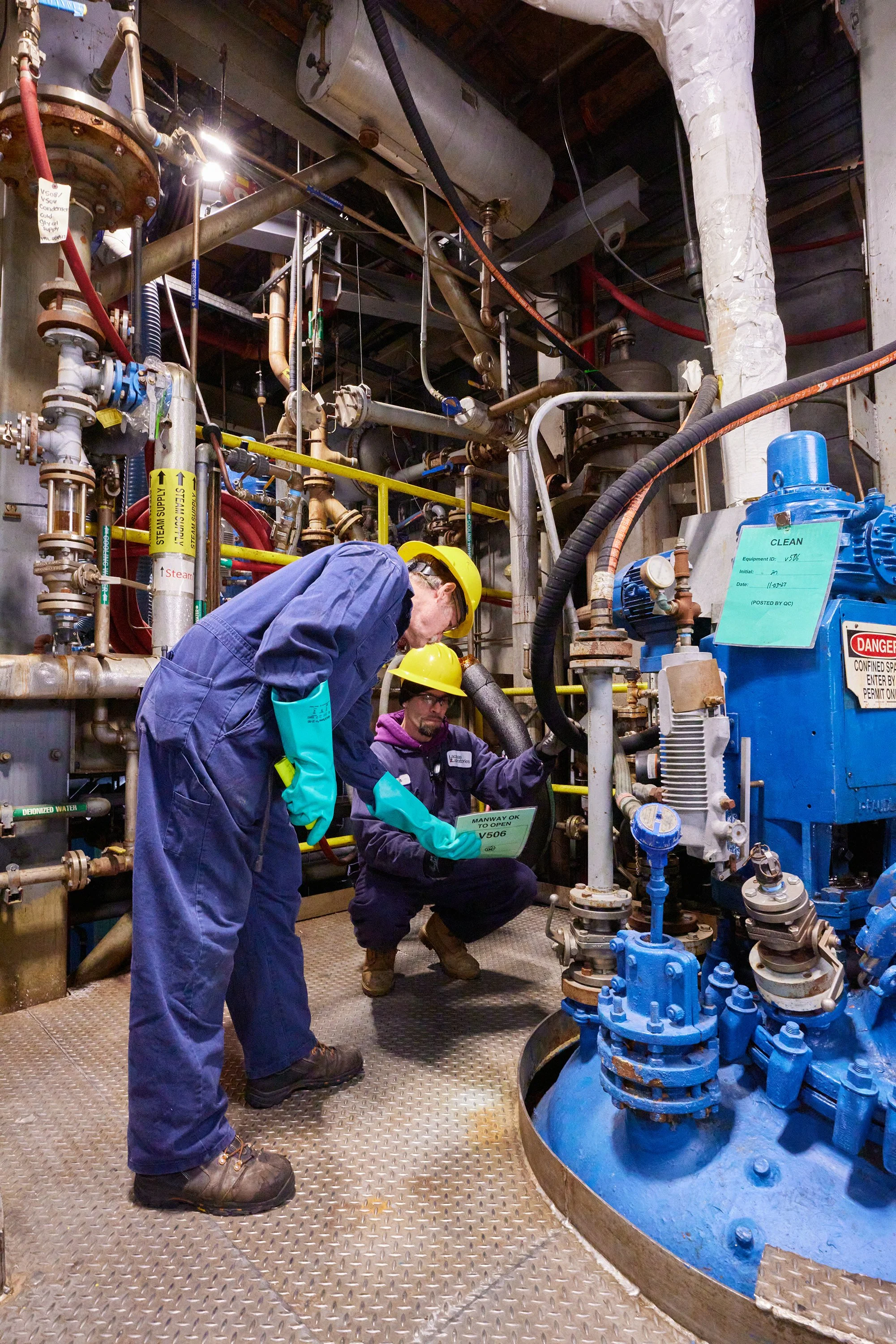 Workers wearing safety gear inspecting and working on industrial plumbing and machinery in a mechanical room.