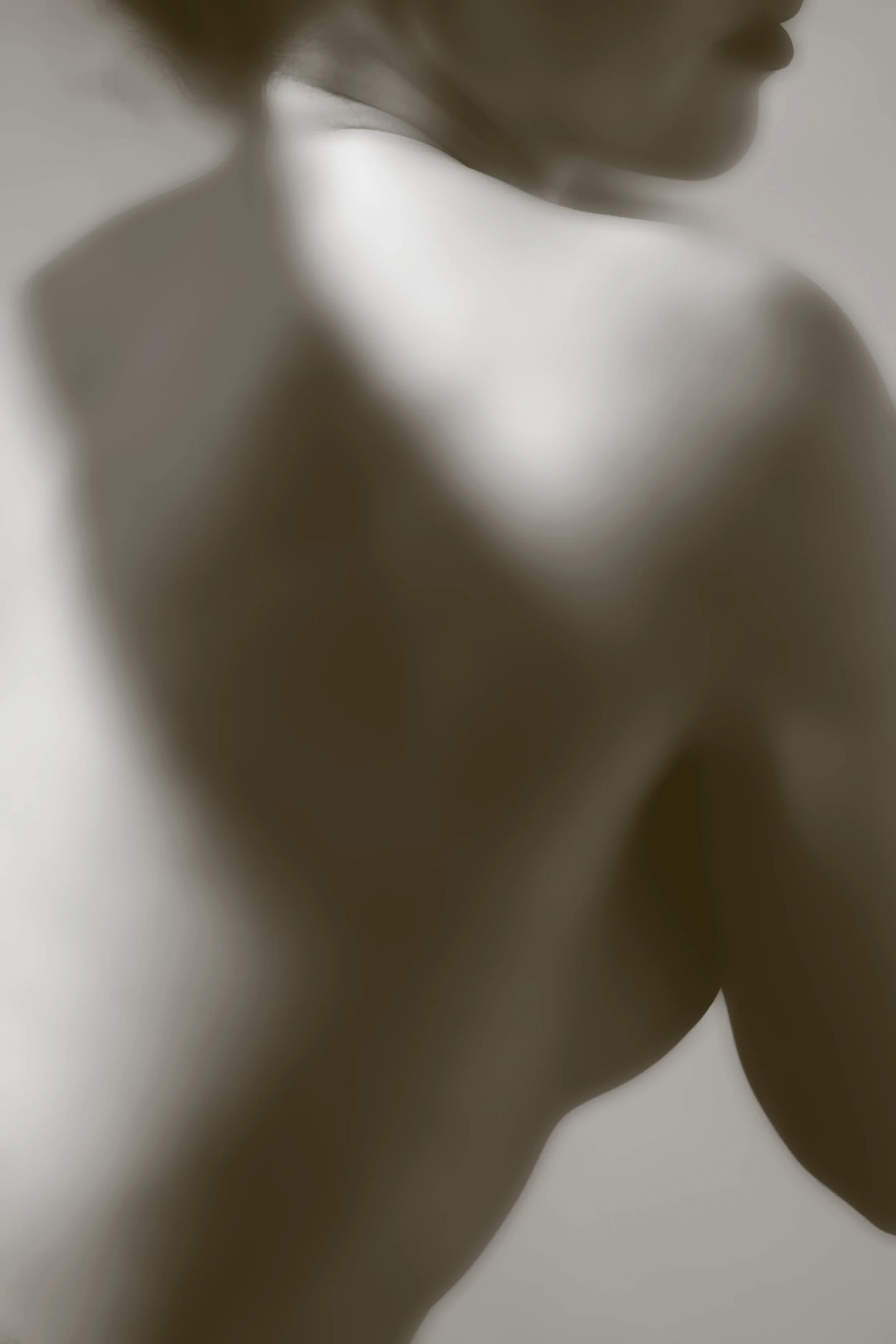 Close-up of a woman's neck and shoulder with soft, diffused lighting, and blurred facial features.