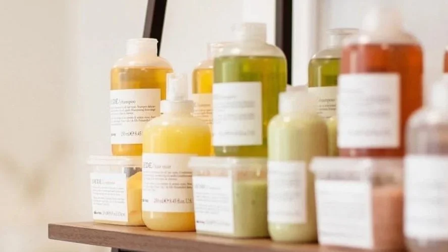 Collection of shampoo and conditioner bottles in various pastel colors on a wooden shelf.
