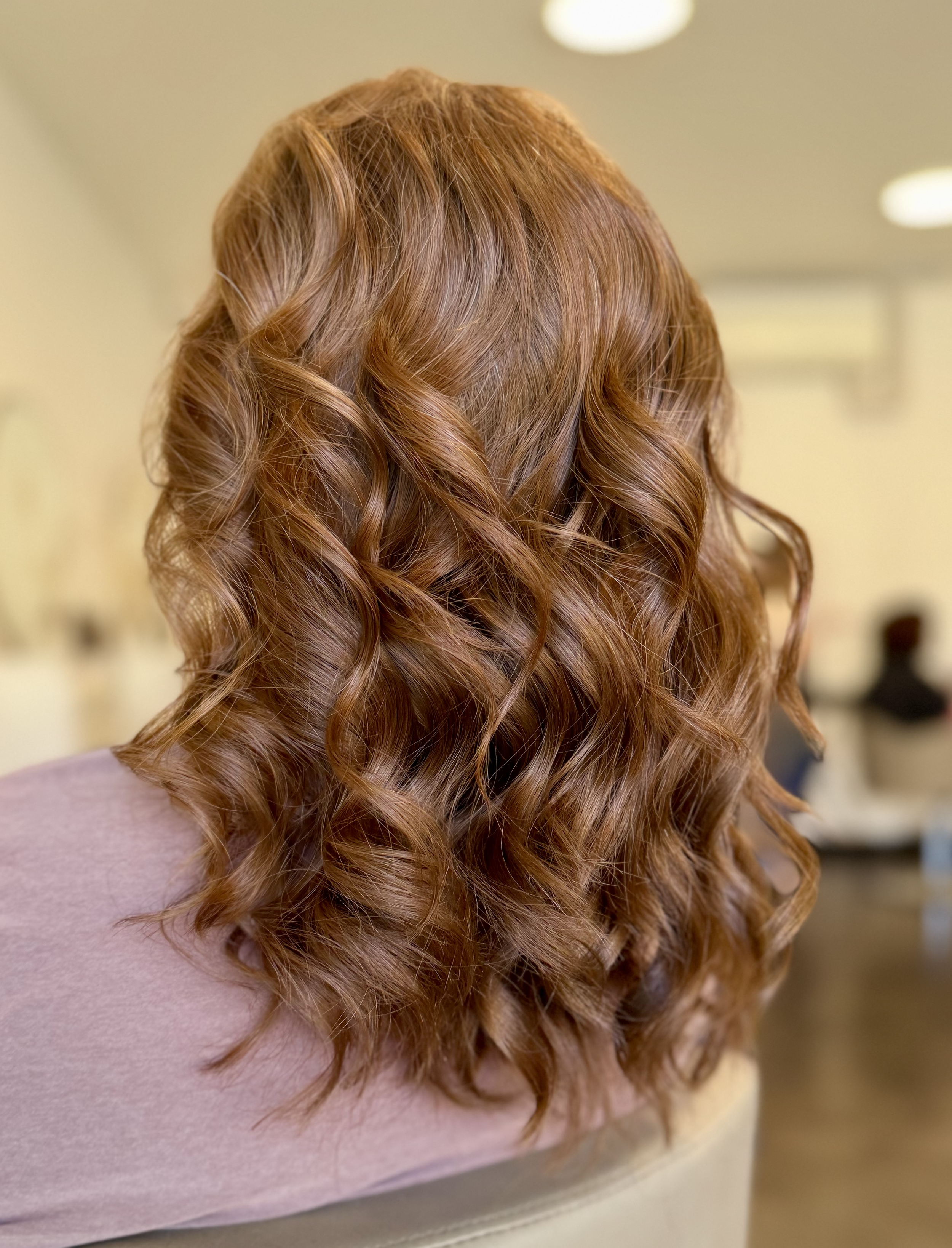 Back of woman's head showing styled, wavy, reddish-brown hair with highlights.