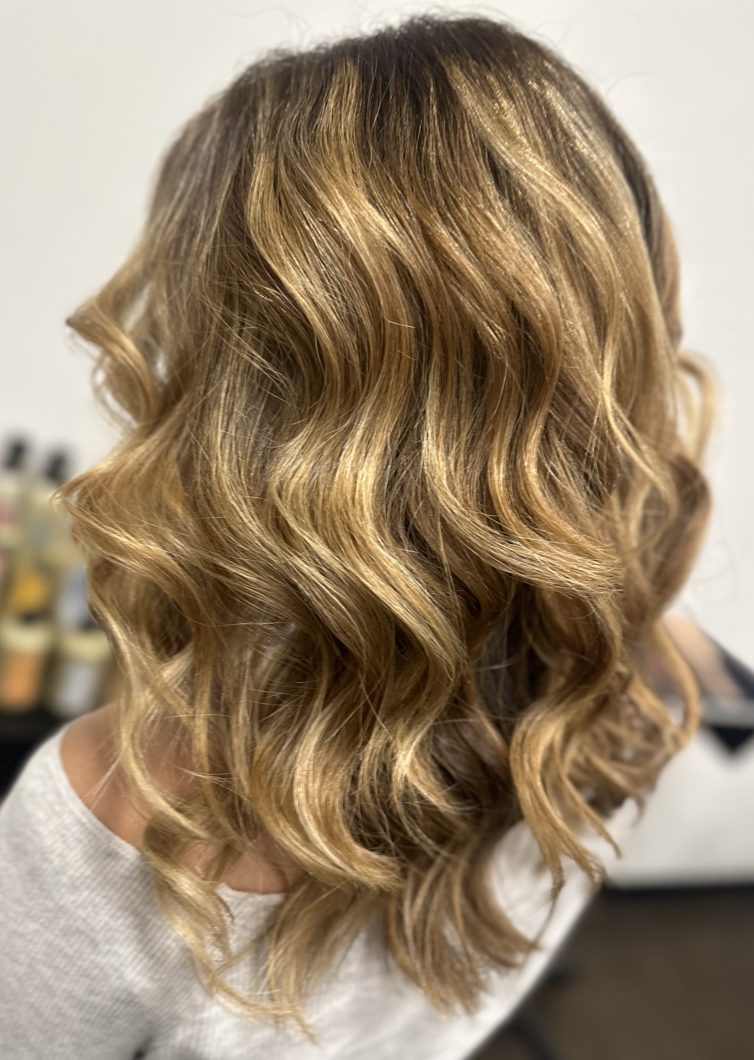 Close-up of a woman's head showing long, wavy blonde hair with highlights, styled in loose curls.