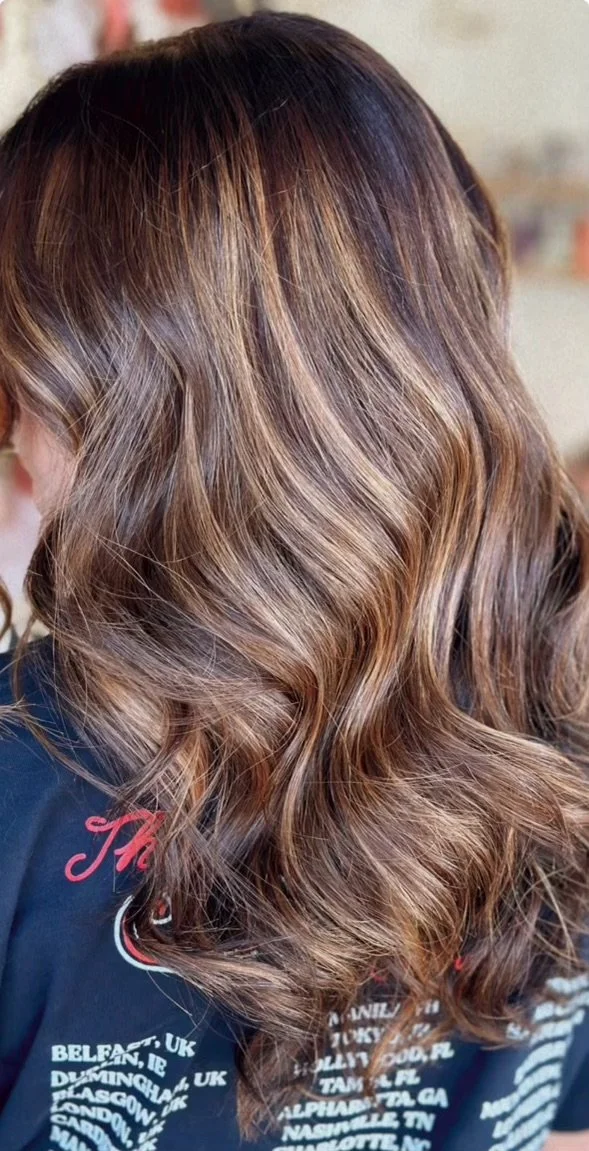Close-up of a woman with long, wavy, ombre hair in shades of brown and blonde.