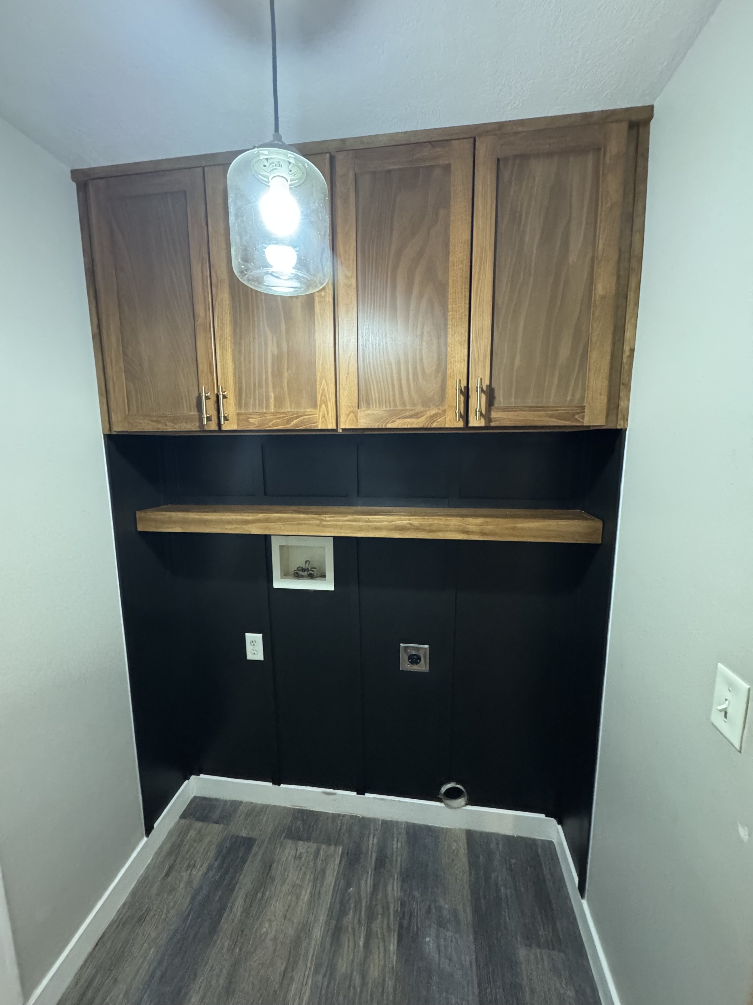 A kitchen cabinet with four wooden doors, an under-cabinet space, a wall with outlets and a framed photo, and a gray and brown striped carpet on the floor.