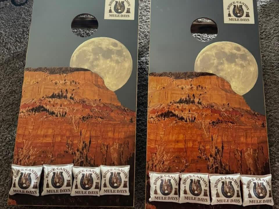 Colorful carnival game boards featuring a landscape image of red rock cliffs, a large full moon, and a dark sky with clouds. Each board has five small candy packages labeled 'Bryce Canyon Mule Days' at the bottom.