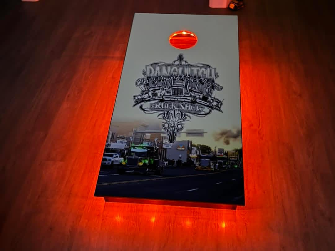 A rectangular signboard with red backlit lighting, featuring the words 'Downtown Charity Truck Show' and illustrations of trucks and city buildings.