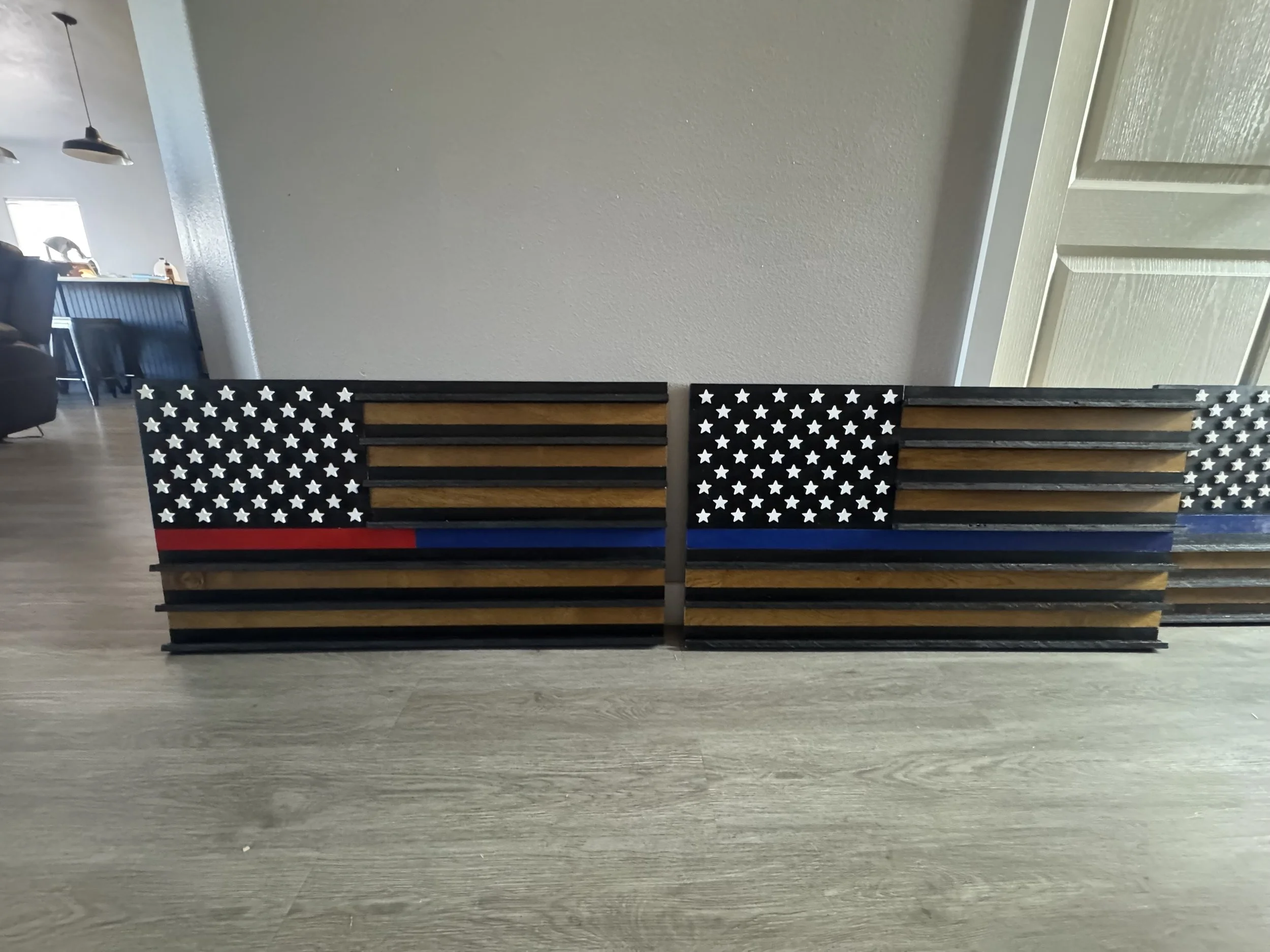 Two wooden benches painted to resemble the American flag, with stars and stripes, placed in front of a plain wall in a room with wooden flooring.