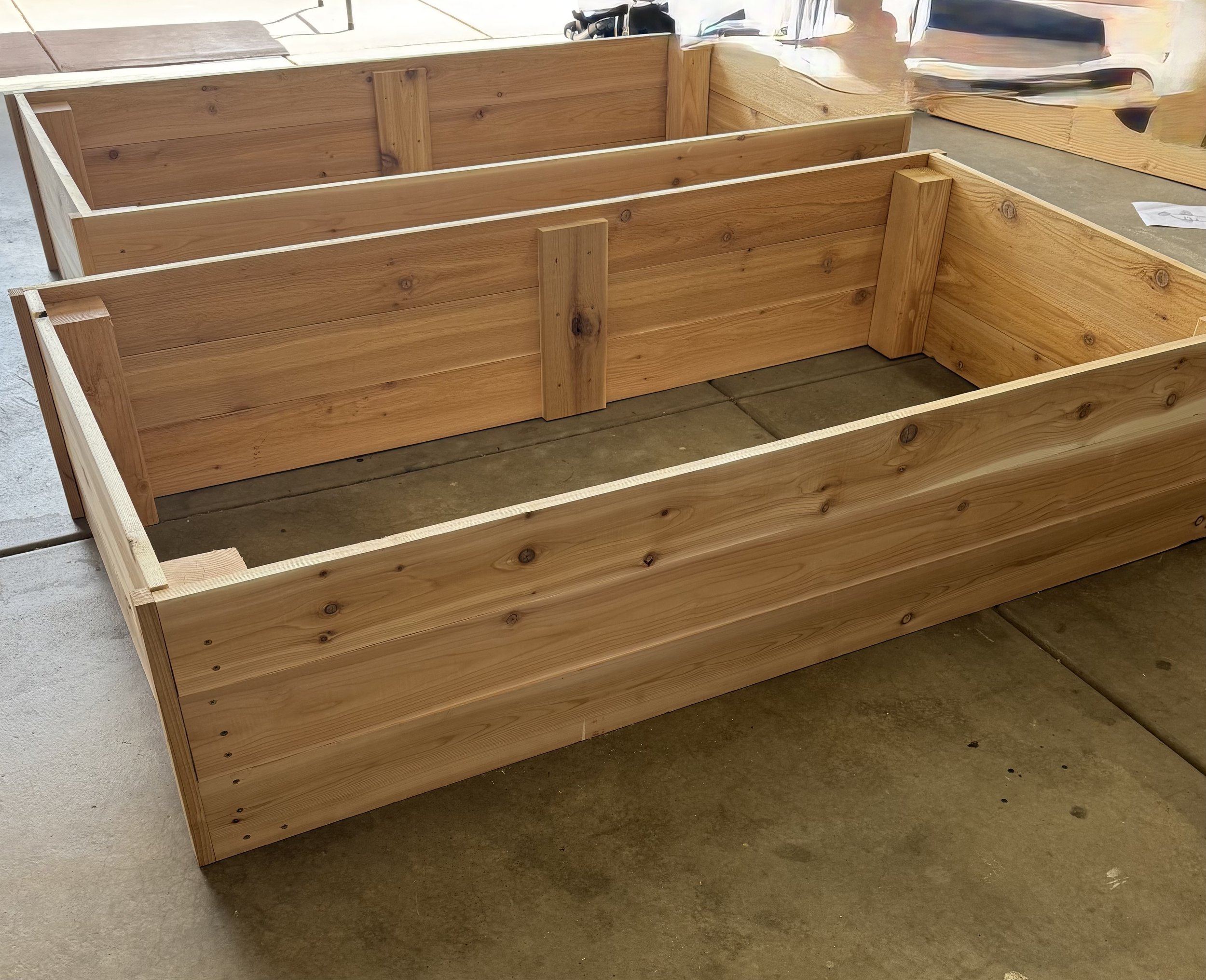 Three unfinished wooden planters on a concrete floor.