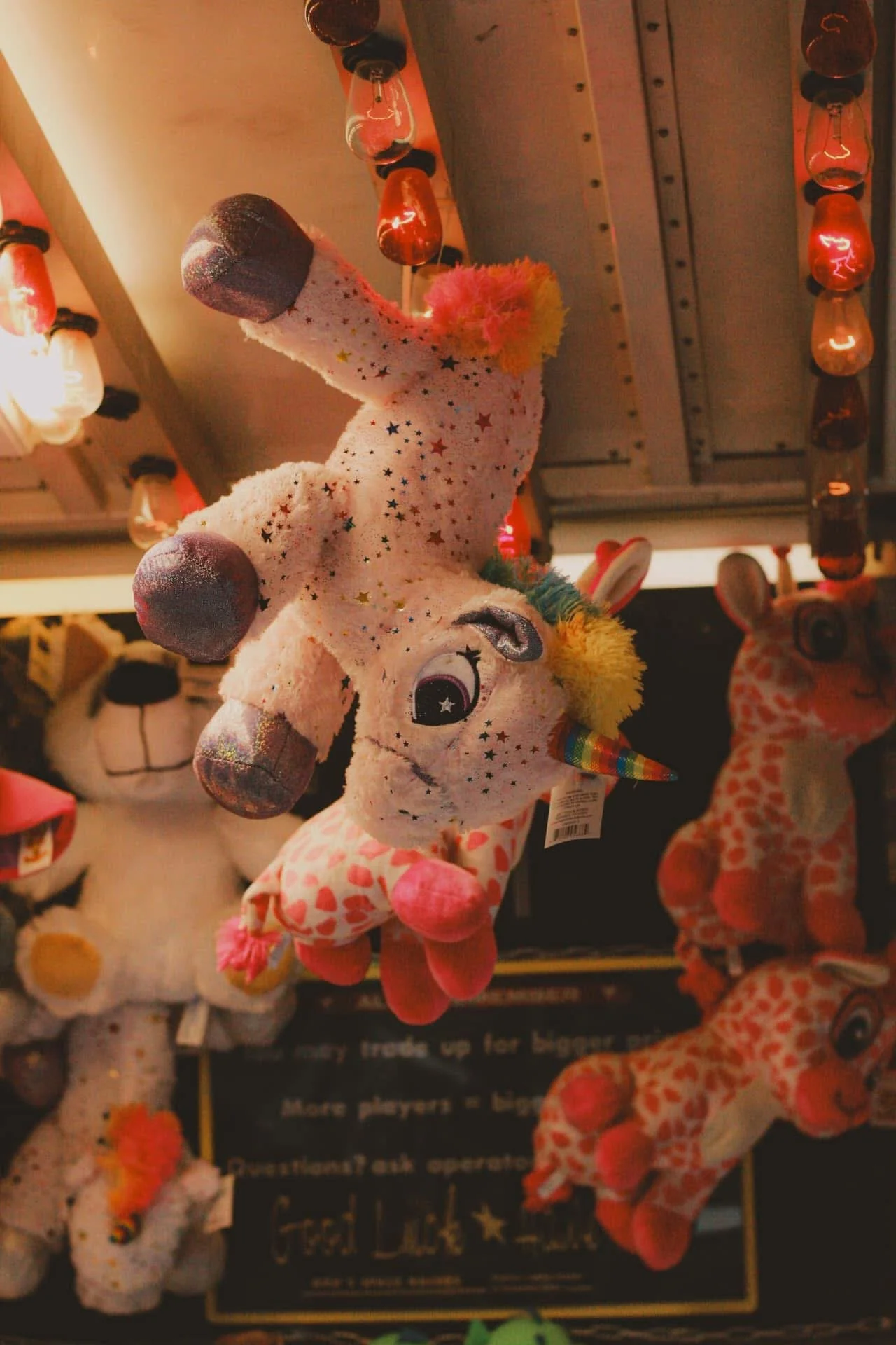 Colorful plush unicorn toy hanging from a store display, surrounded by other stuffed animals.